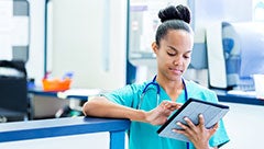 The role of organizations in shaping physician use of electronic health records. Stock image shows a female clinician in scrubs holding and looking at a tablet computer