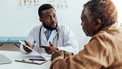 Investigation of the role of perceived access to primary care in mediating and moderating racial and ethnic disparities in chronic disease control in the veterans health administration. Stock image of a black clinician in white coat sitting with an elderly black patient