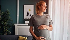 Maternal chronic hypertension in women veterans . Stock image shows a pregnant woman standing in a living room holding her stomach.