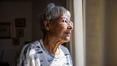Access to preferred skilled nursing facilities: Transitional care pathways for patients with Alzheimer's disease and related dementias. Stock image shows elderly woman standing at a window staring out