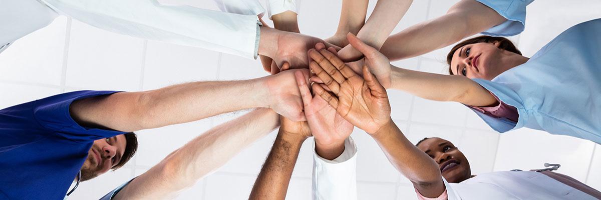 health care workers stand in team huddle circle with stacked hands