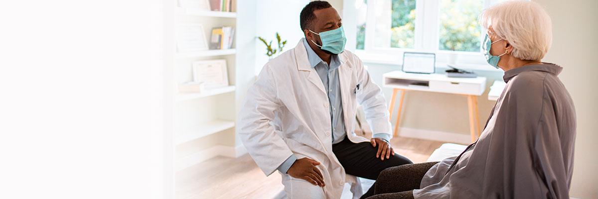 Black male physician sits opposite an elderly white patient in a bright office